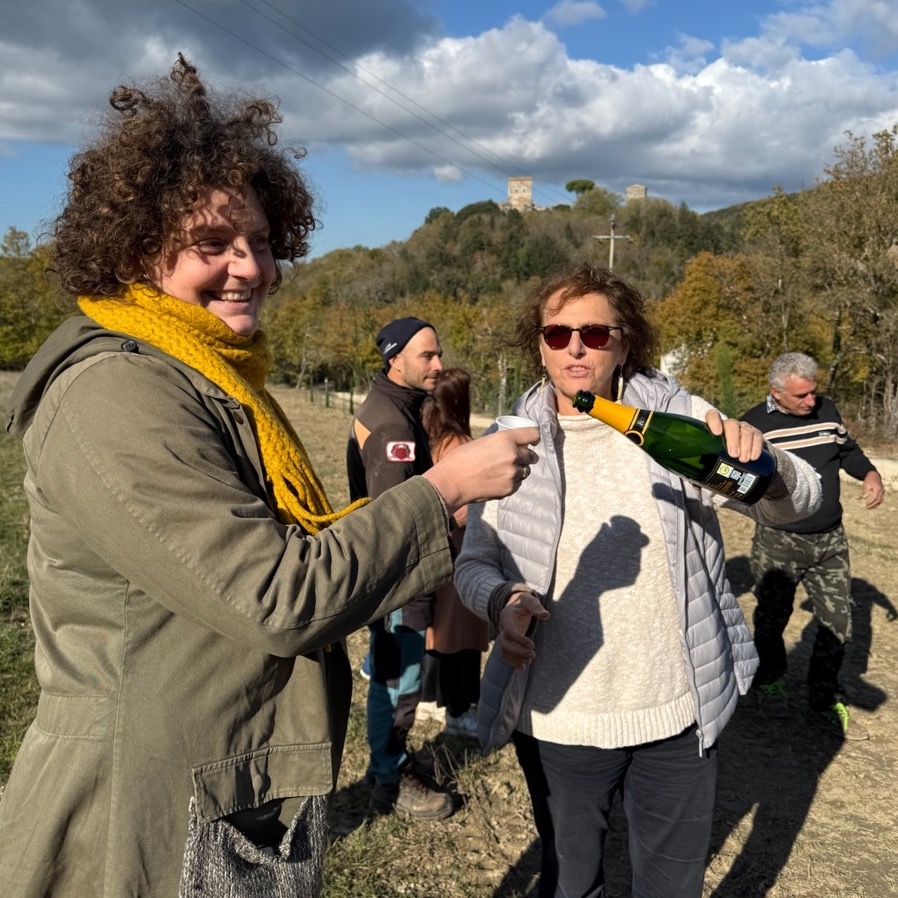 Daniela, a staff members, pours sparkling wine into a cup held up by Silvia, another staff member (and her daughter). Other staff members are in the background.